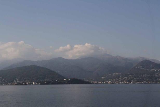 Blick über einen See auf bewaldete Berge und kleine Städte.