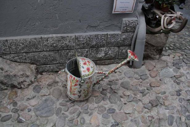Eine dekorative Gießkanne mit Blumenmuster steht auf einem Pflasterweg.