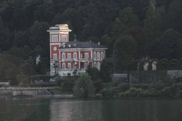 Eine rote Villa mit Turm steht am Ufer eines Sees.
