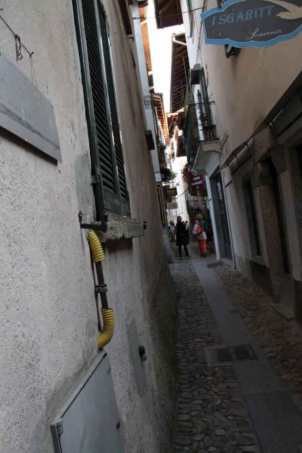 Blick in eine schmale Gasse mit Kopfsteinpflaster und einigen Passanten.