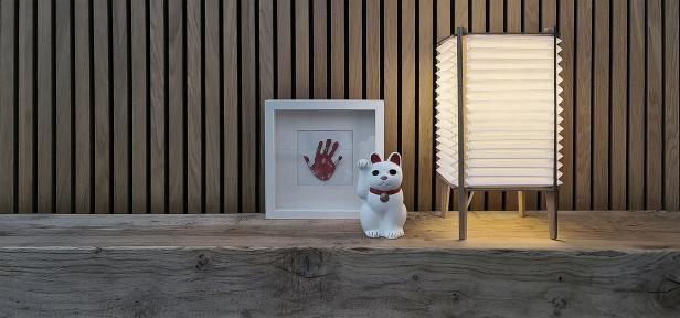 Eine Maneki-Neko-Glückskatze steht neben einem gerahmten Handabdruck und einer Lampe auf einem Holzregal.