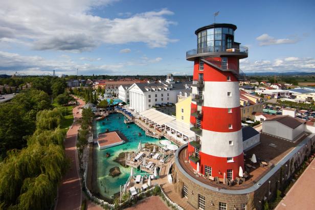 Ein rot-weiß gestreifter Leuchtturm überblickt ein Resort mit künstlichen Wasserwegen.