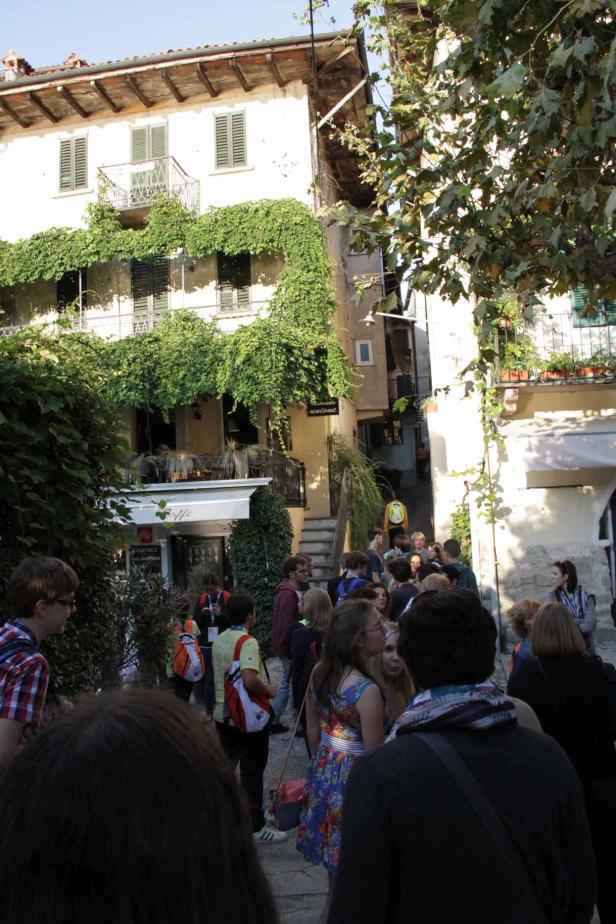 Eine Menschenmenge versammelt sich in einer Gasse vor einem mit Efeu bewachsenen Gebäude.