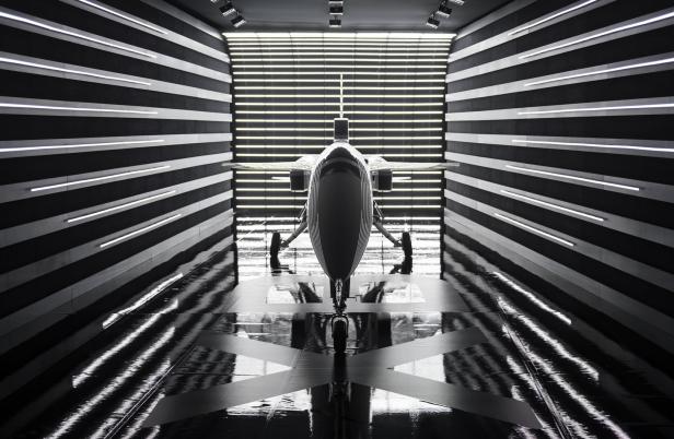 Ein futuristisches Flugzeug steht in einem Raum mit Schwarz-Weiß-Streifen und Neonbeleuchtung.