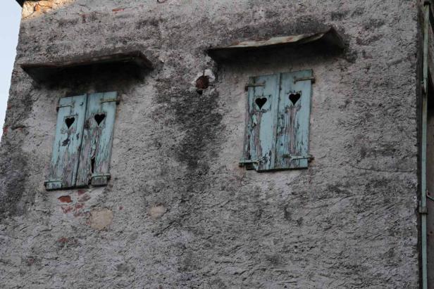 Zwei Fenster mit herzförmigen Ausschnitten in alten, blauen Fensterläden.