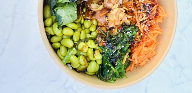 Eine Schüssel mit Edamame, Algensalat, Karotten und mariniertem Fisch.