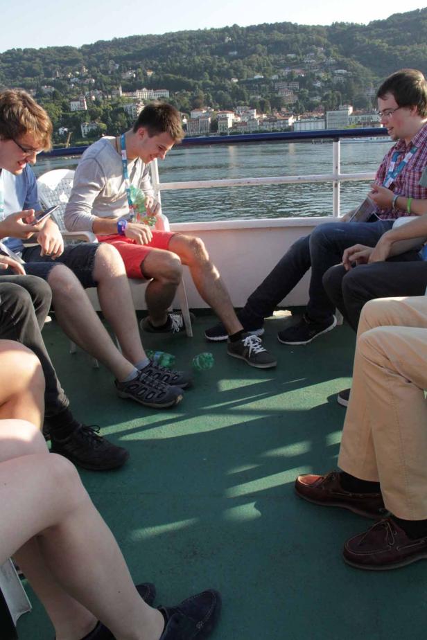 Eine Gruppe junger Leute sitzt auf einem Boot mit Blick auf eine bewaldete Küstenlinie.