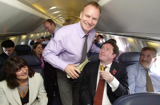 Sting serviert Piers Morgan und anderen Passagieren Champagner in einem Flugzeug.