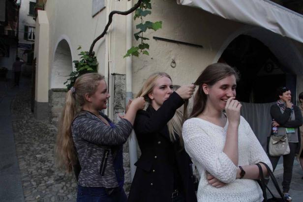 Drei junge Frauen stehen auf der Straße, eine flechtet der anderen die Haare.