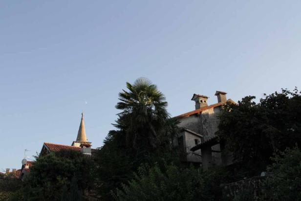 Eine Kirchturmspitze und ein Haus mit Palmen unter blauem Himmel.