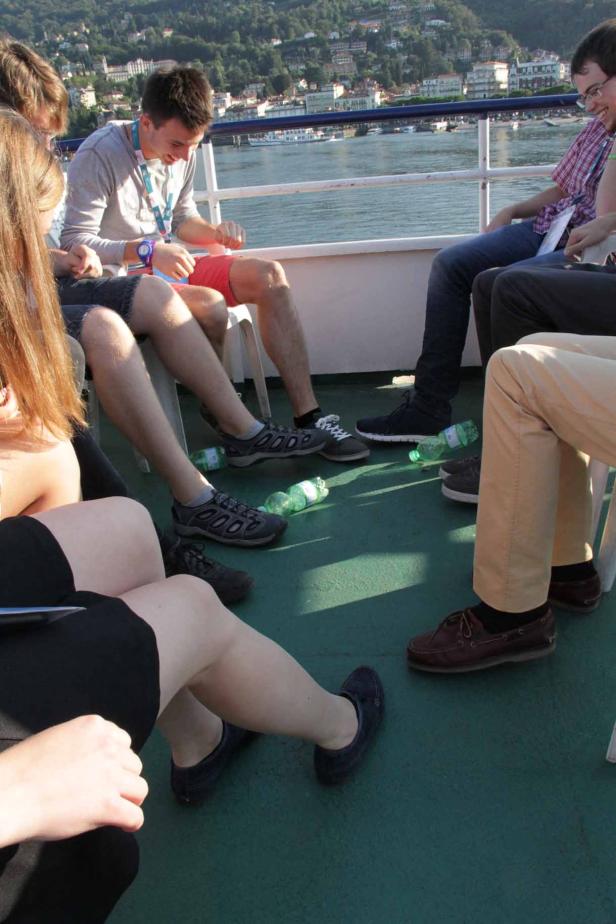 Eine Gruppe von Menschen sitzt auf einem Schiff mit Blick auf das Wasser und die Stadt im Hintergrund.