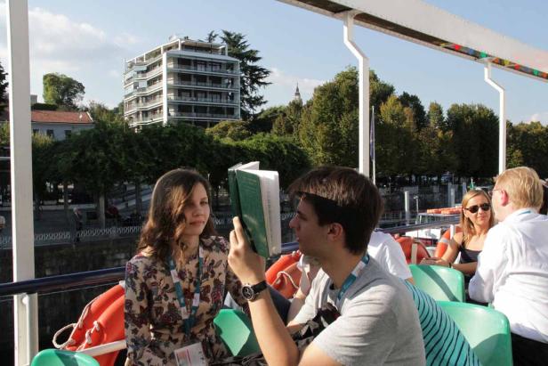 Auf einem Ausflugsschiff liest ein junger Mann ein Buch vor einer jungen Frau.