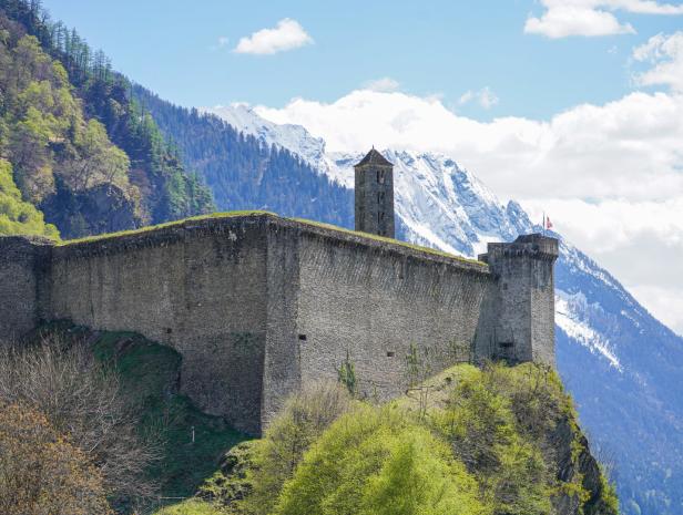 Eine mittelalterliche Burg thront auf einem Hügel vor schneebedeckten Bergen.
