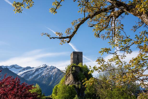 Ein mittelalterlicher Turm thront auf einem Felsen vor schneebedeckten Bergen.
