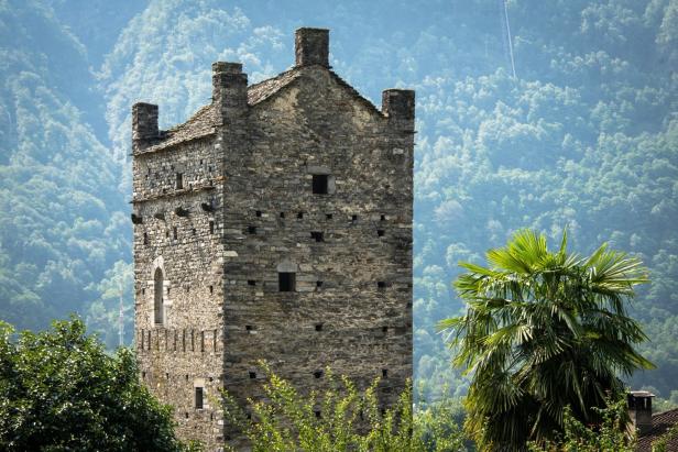 Ein mittelalterlicher Steinturm steht vor einem bewaldeten Hügel.