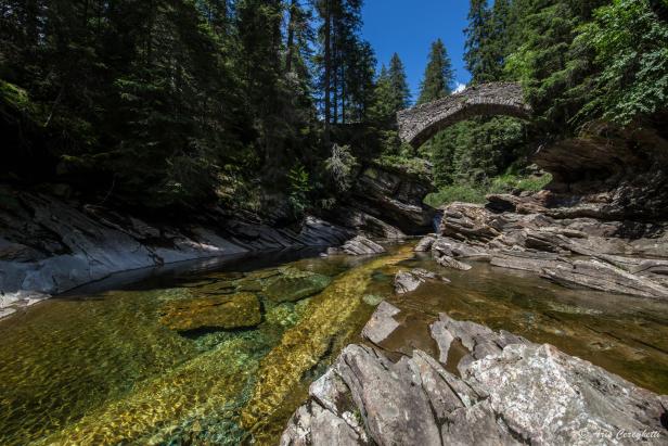 Eine Steinbrücke überspannt einen klaren Fluss in einer bewaldeten Schlucht.