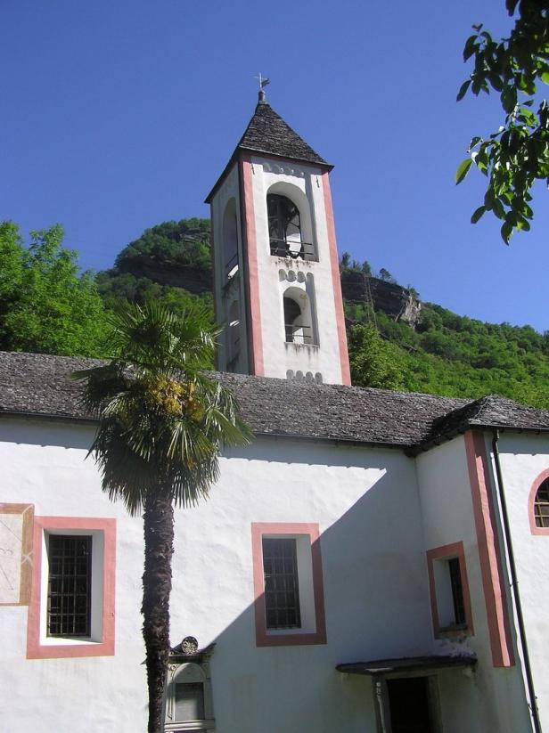 Ein Kirchturm mit einer Palme davor unter blauem Himmel.