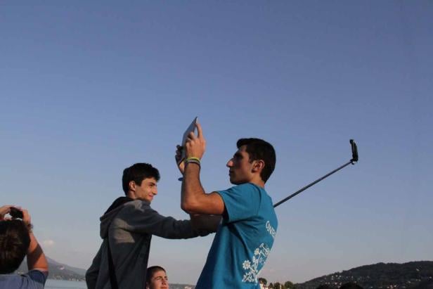 Eine Gruppe junger Leute macht Fotos mit einem Tablet und einem Selfie-Stick im Freien.