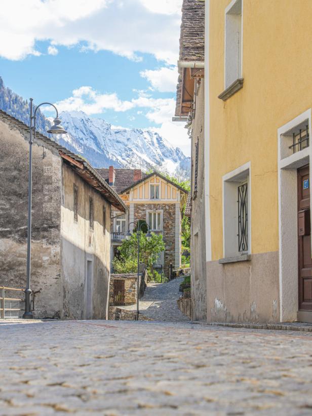 Eine Gasse mit Kopfsteinpflaster führt zu schneebedeckten Bergen.