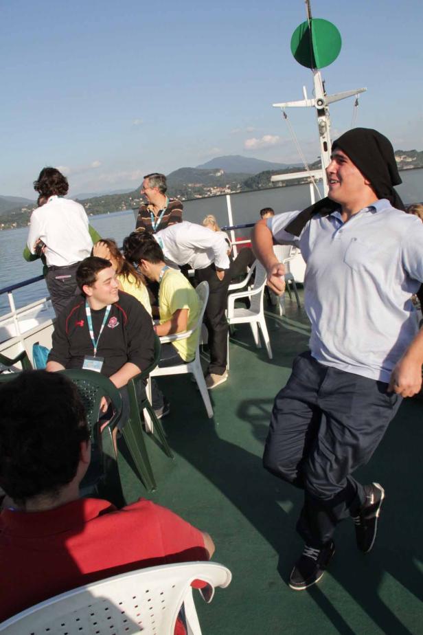 Ein Mann tanzt auf einem Schiff, während andere Passagiere sitzen und stehen.