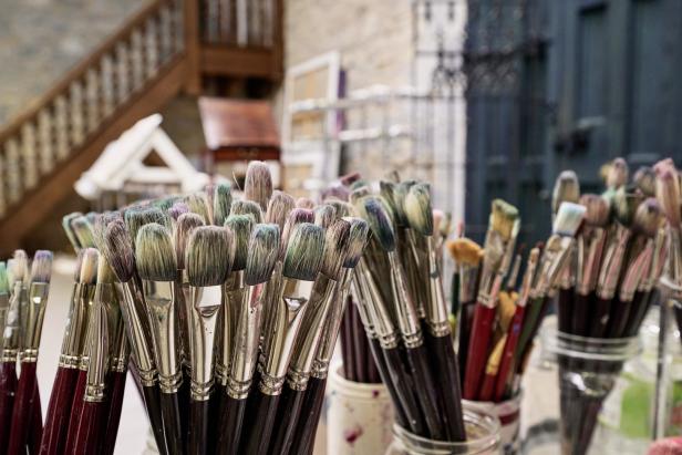 Viele benutzte Pinsel stehen in Gläsern in einem Atelier.