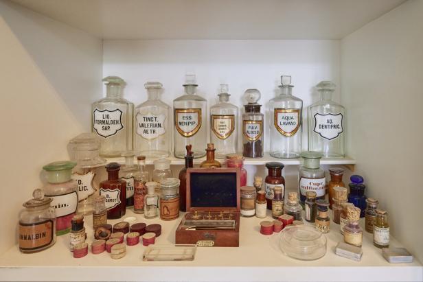 Regale mit alten Apothekerflaschen und -utensilien, einige mit lateinischen Beschriftungen wie „Aqua Lavand“.