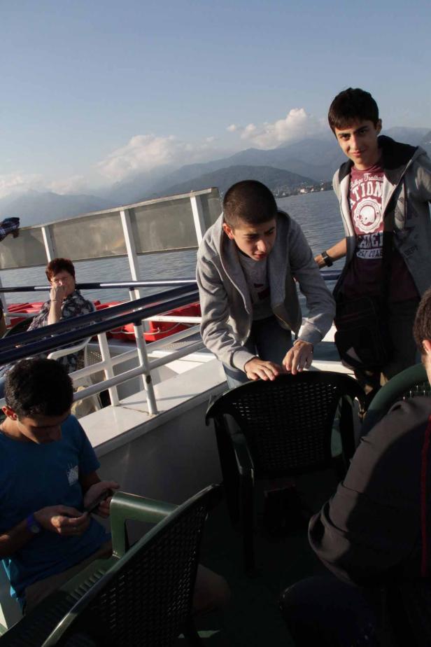 Eine Gruppe junger Leute auf einem Schiff mit Bergen im Hintergrund.