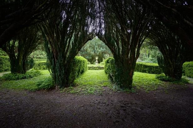 Ein formaler Garten mit geschnittenen Hecken und einem dekorativen Brunnen im Hintergrund.