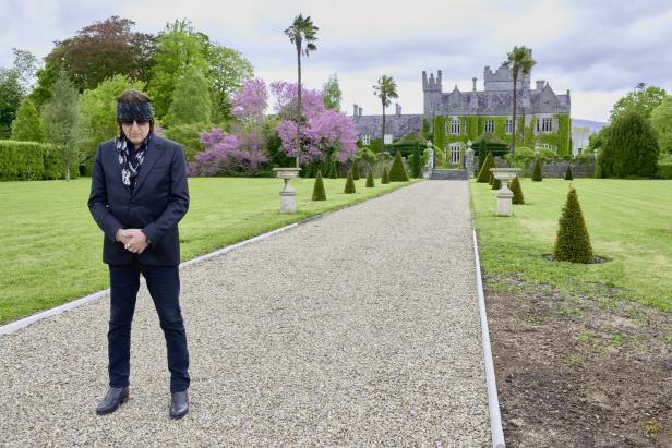 Ein Mann mit Sonnenbrille steht vor einem Schlossgarten.