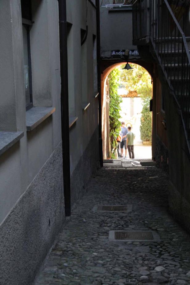 Blick durch einen schmalen Durchgang mit Kopfsteinpflaster auf zwei Personen.