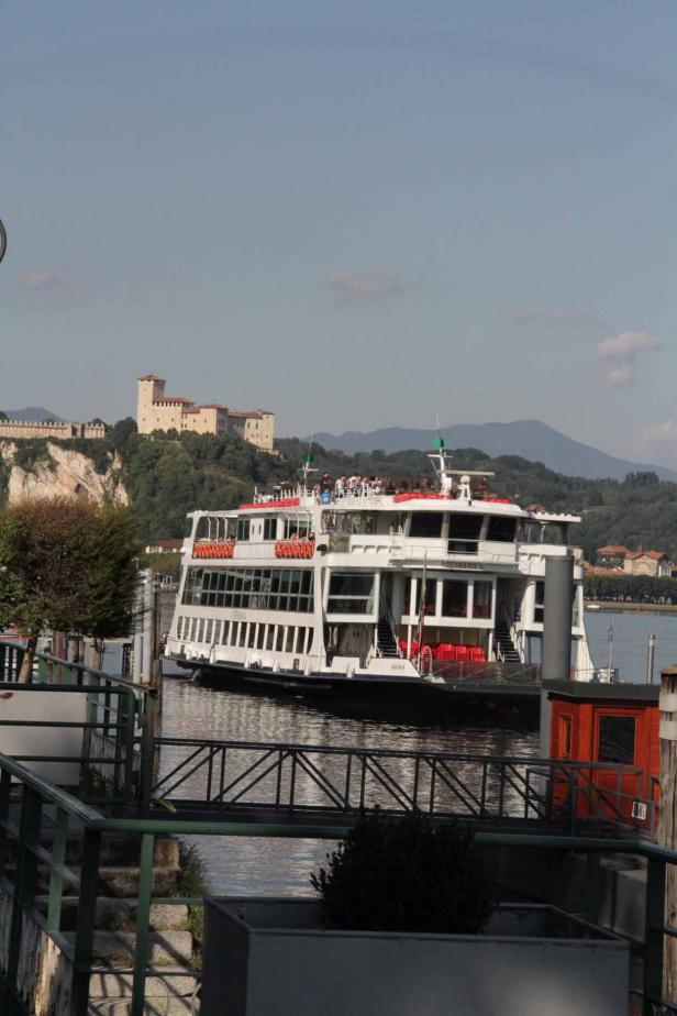 Eine Fähre legt am Ufer des Lago Maggiore an, im Hintergrund die Rocca di Angera.