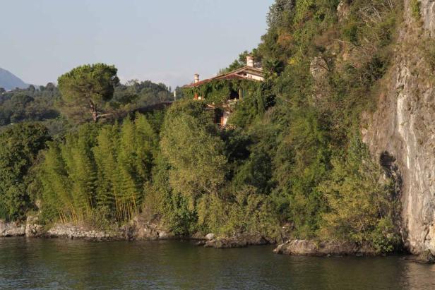 Ein Haus, teilweise mit Efeu bewachsen, steht auf einem bewaldeten Hügel am Wasser.