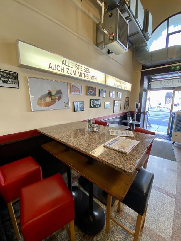 Innenansicht eines Cafés mit Tischen und Stühlen, sowie Speisekarten und Zeitungen.