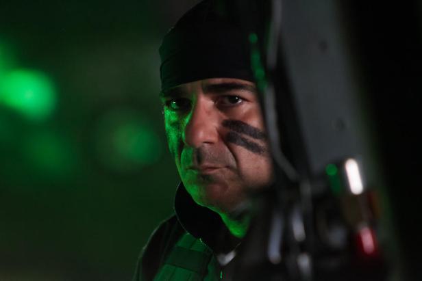 Ein Mann mit Kriegsbemalung und schwarzer Mütze blickt ernst in die Kamera.