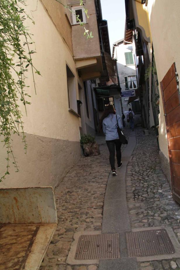 Eine Frau geht eine enge Gasse mit einem „Ristorante Pizzeria“-Schild entlang.