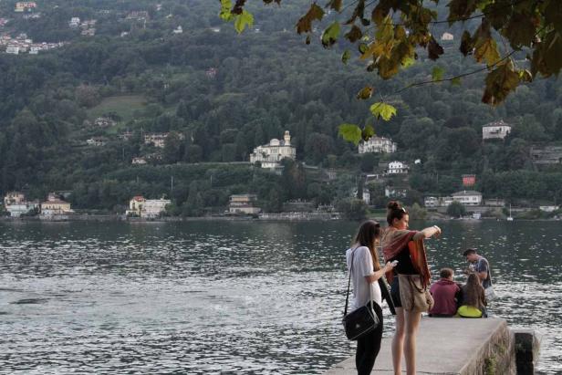 Eine Gruppe von Menschen sitzt an einem See mit Häusern am bewaldeten Hang.