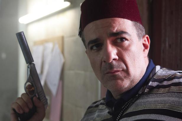 Ein Mann mit Fez hält eine Pistole in der Hand.