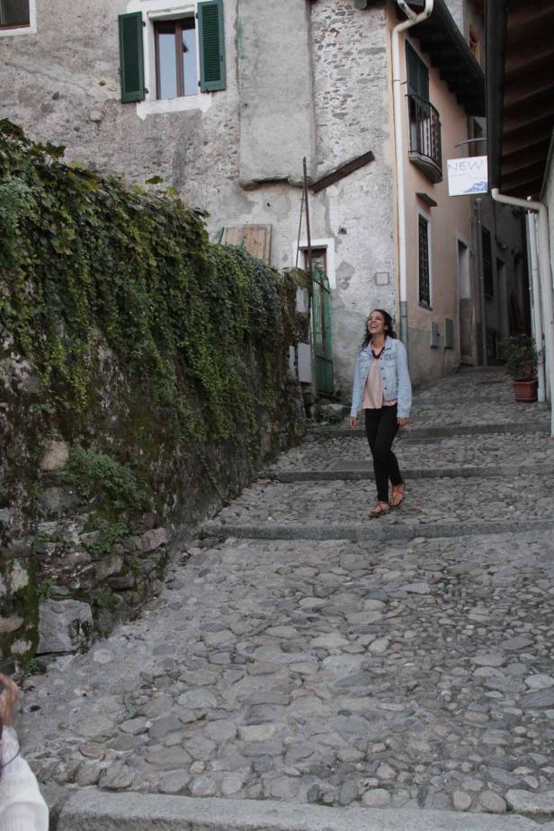 Eine junge Frau geht eine steile Steintreppe in einer malerischen Gasse hinunter.