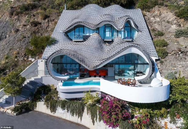 Ein modernes Haus mit geschwungenem Dach und Pool an einem Hang.