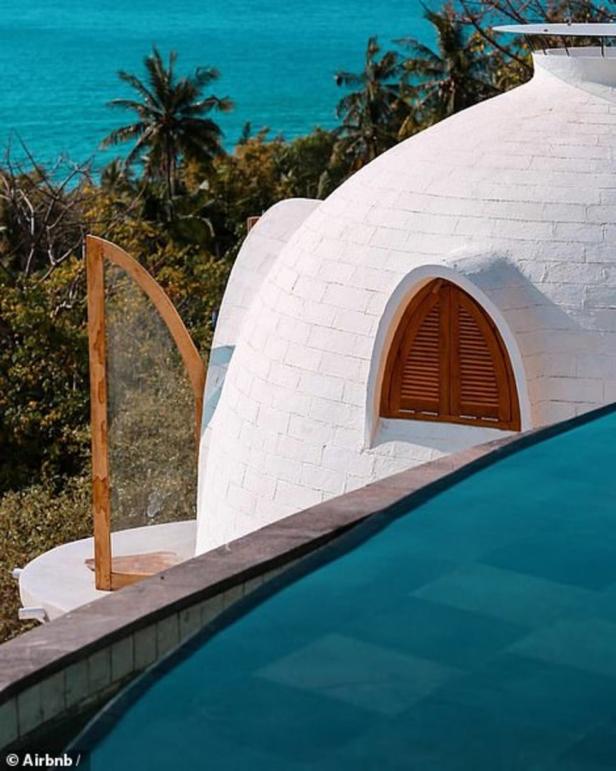 Ein weißes, kuppelförmiges Gebäude mit einem Pool im Vordergrund und Meer im Hintergrund.