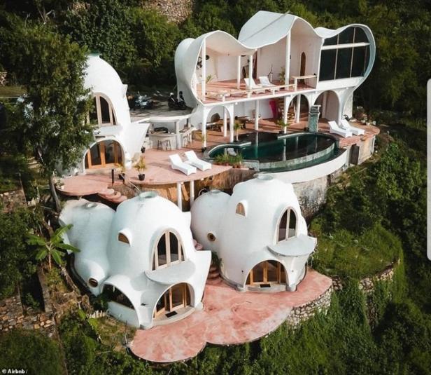 Ein ungewöhnliches, weißes Haus mit Kuppeln und einem Pool liegt auf einem grünen Hügel.