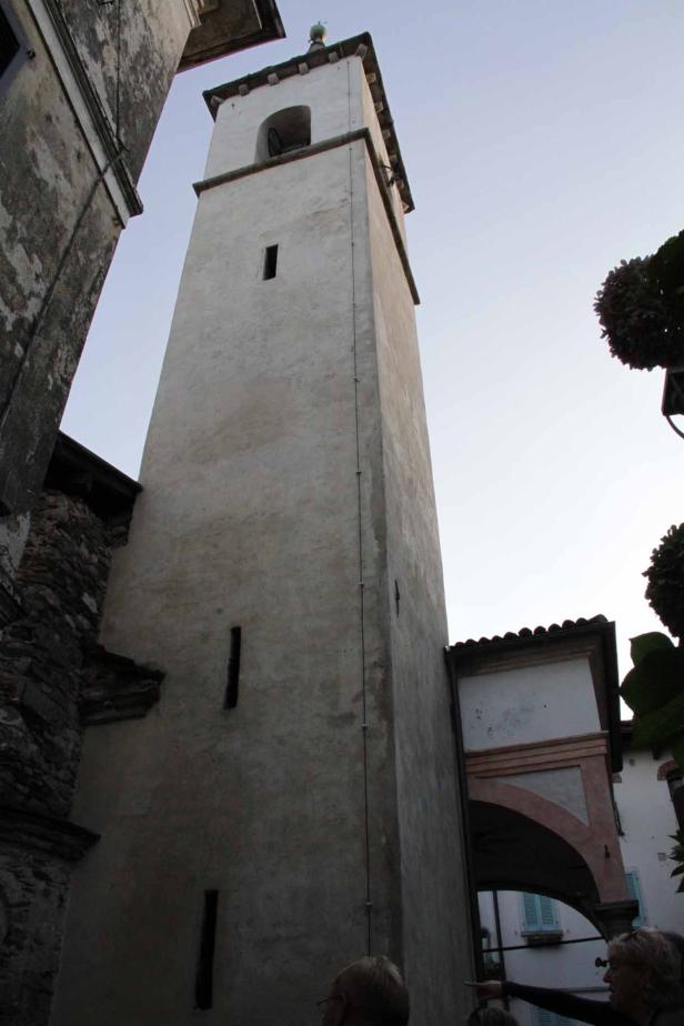 Ein hoher Kirchturm aus Stein mit kleinen Fenstern erhebt sich in den Himmel.
