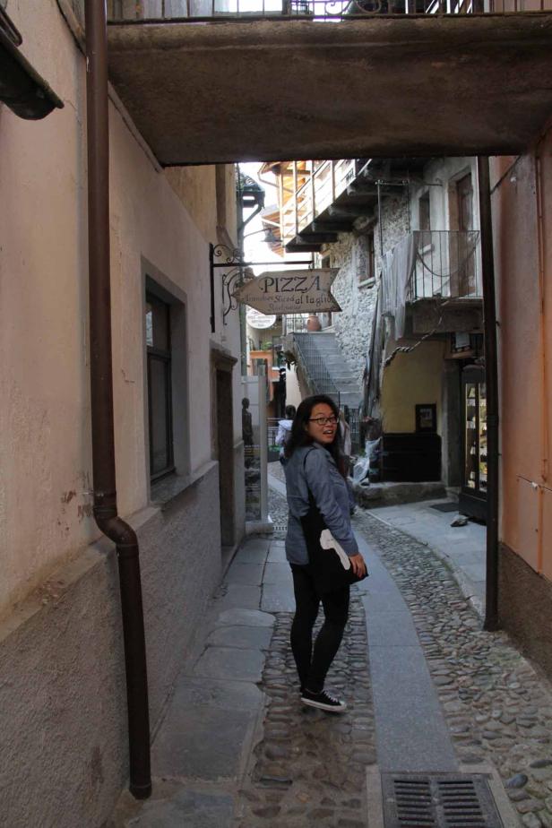 Eine Frau geht durch eine enge Gasse mit einem Pizza-Restaurant im Hintergrund.