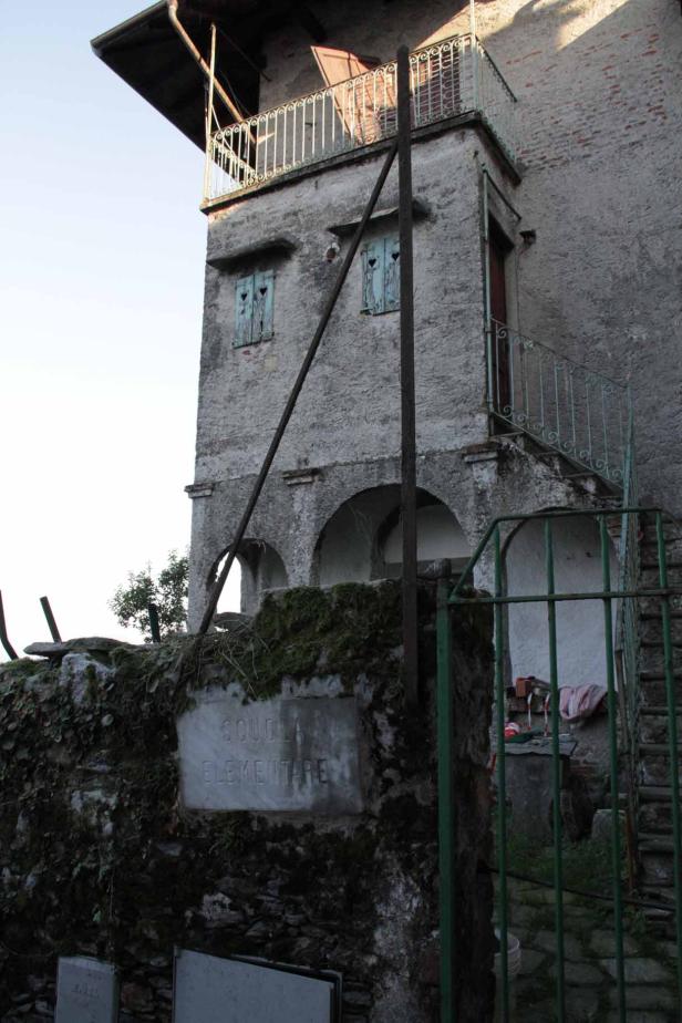 Ein altes, graues Gebäude mit einem Schild, das „Scuola Elementare“ (Grundschule) anzeigt.