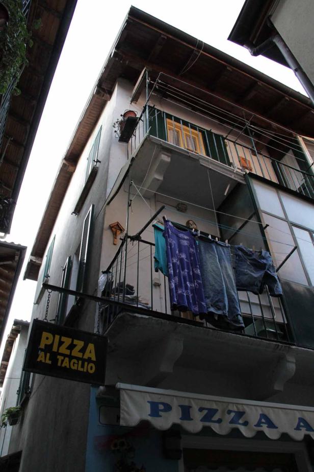 Ein Blick von unten auf ein Gebäude mit einem „Pizza al Taglio“-Schild und Wäsche auf einem Balkon.