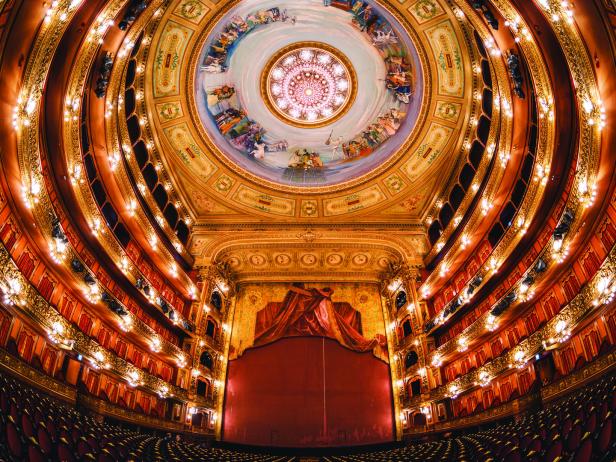 Blick in ein prunkvolles Opernhaus mit rotem Vorhang und Deckenmalerei.