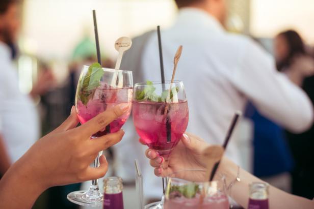Zwei Personen stoßen mit rosafarbenen Cocktails an.