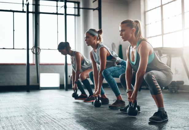 Drei Frauen trainieren mit Kettlebells in einem Fitnessstudio.