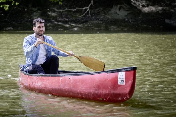 Ein Mann paddelt in einem roten Kanu auf einem ruhigen Gewässer.