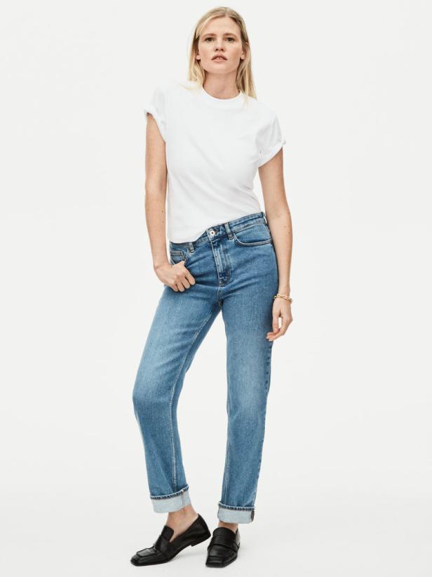 Eine Frau mit blonden Haaren trägt ein weißes T-Shirt, Jeans und schwarze Loafer.